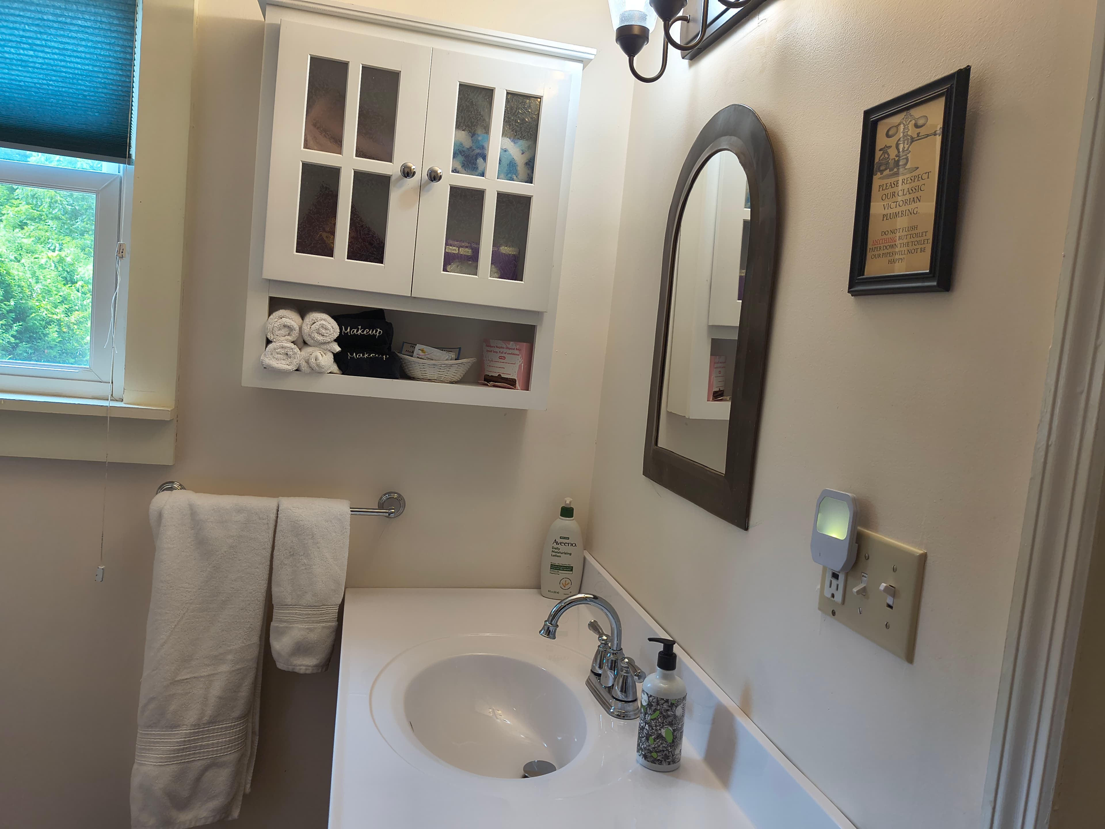 A bright bathroom featuring a sink, mirror, neatly arranged towels, and a wall cabinet.