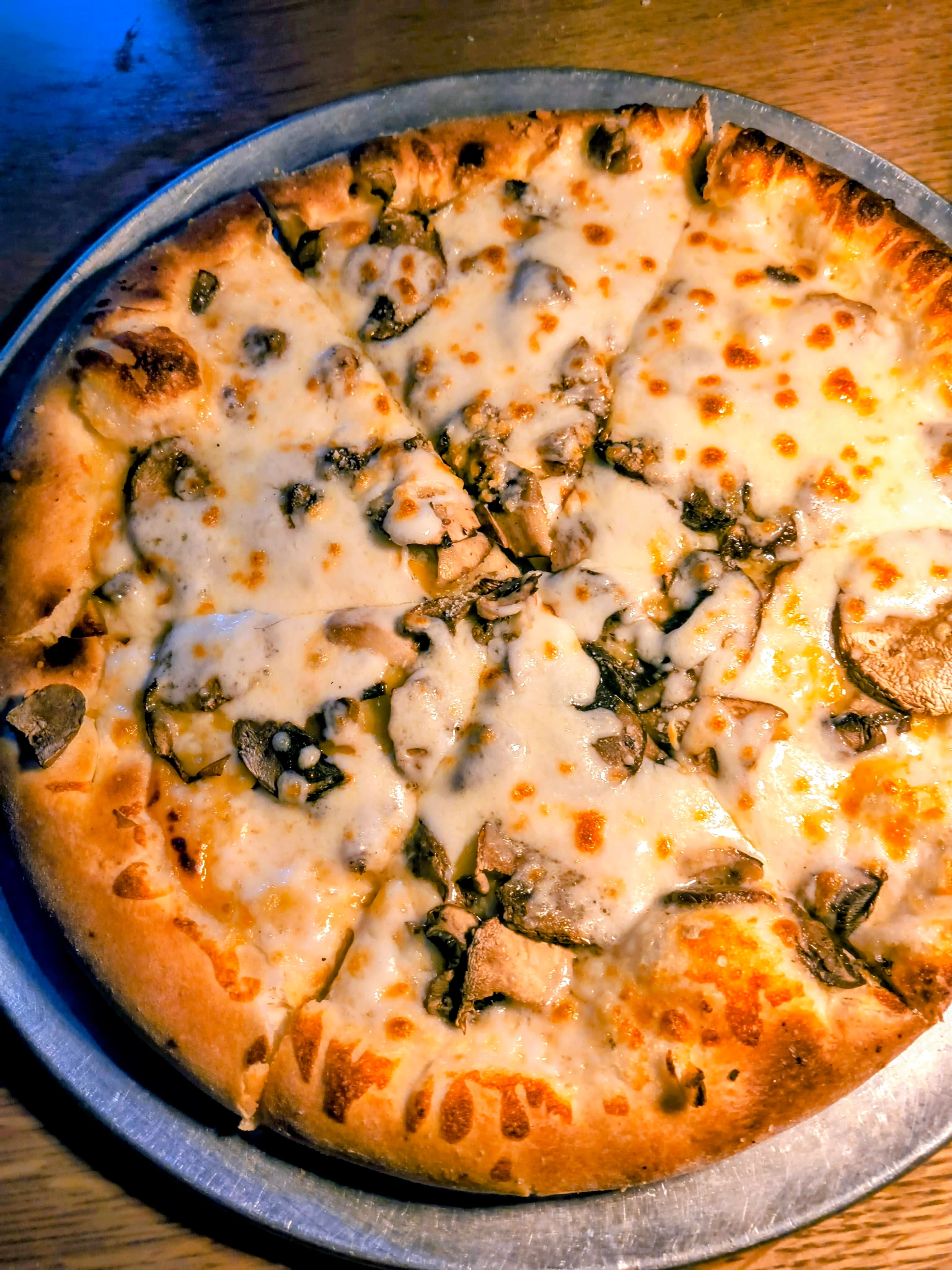 A freshly baked pizza topped with melted cheese and mushrooms, sliced into wedges.