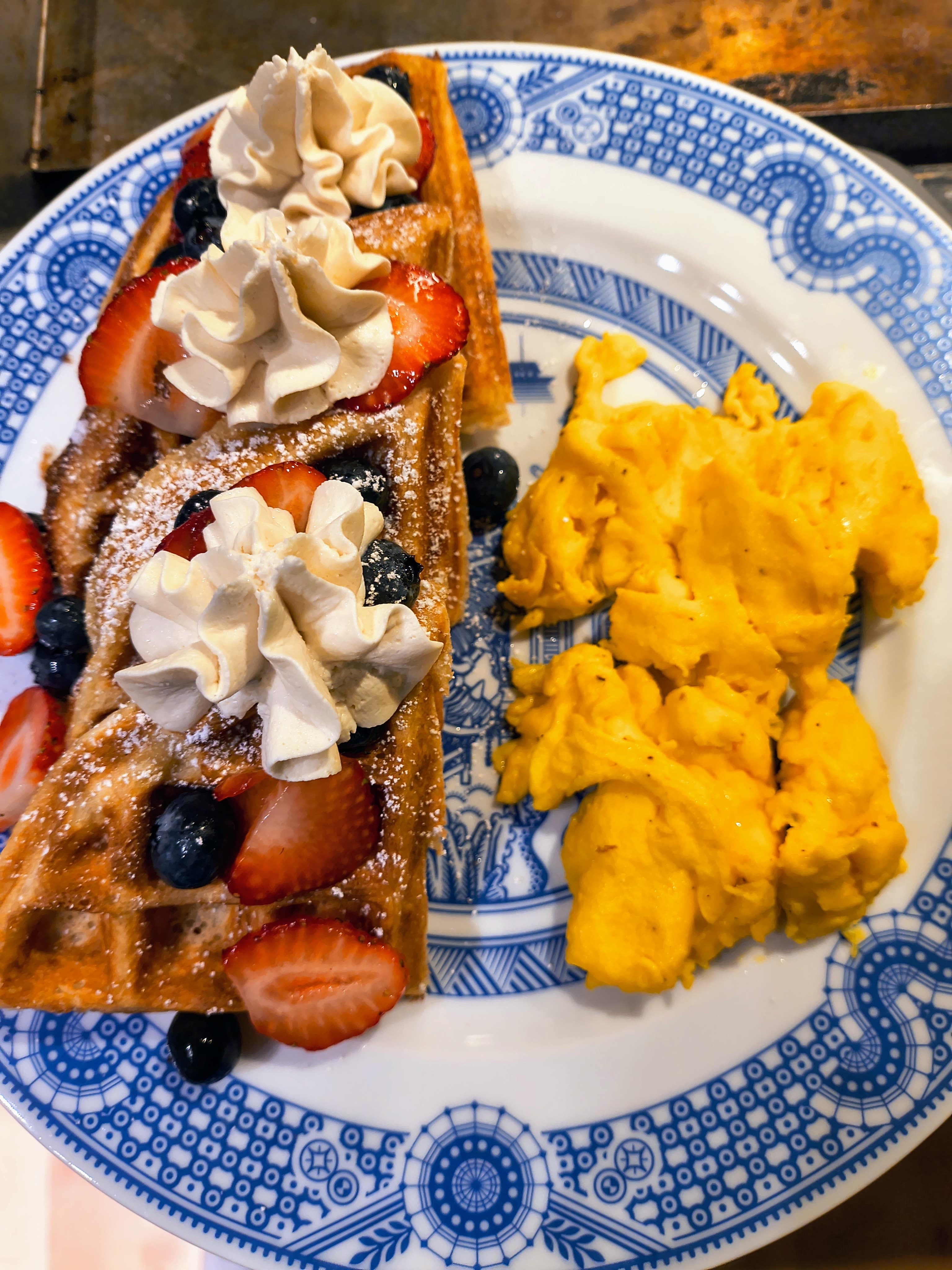 A plate featuring a waffle topped with strawberries, blueberries, and whipped cream, alongside scrambled eggs.