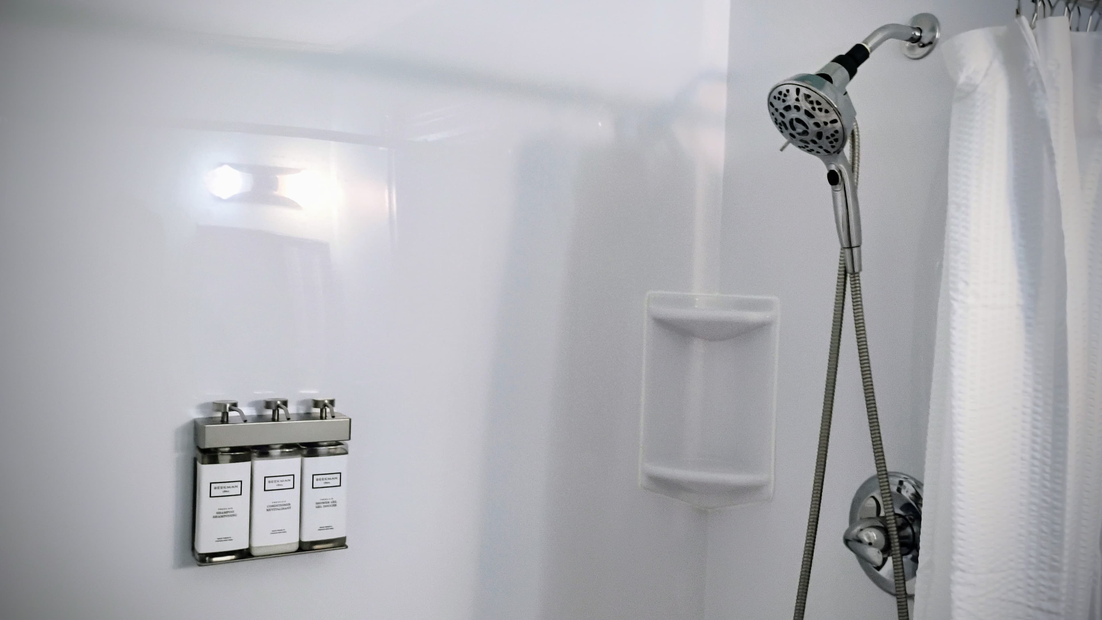 A modern shower featuring a wall-mounted shampoo dispenser and handheld showerhead.