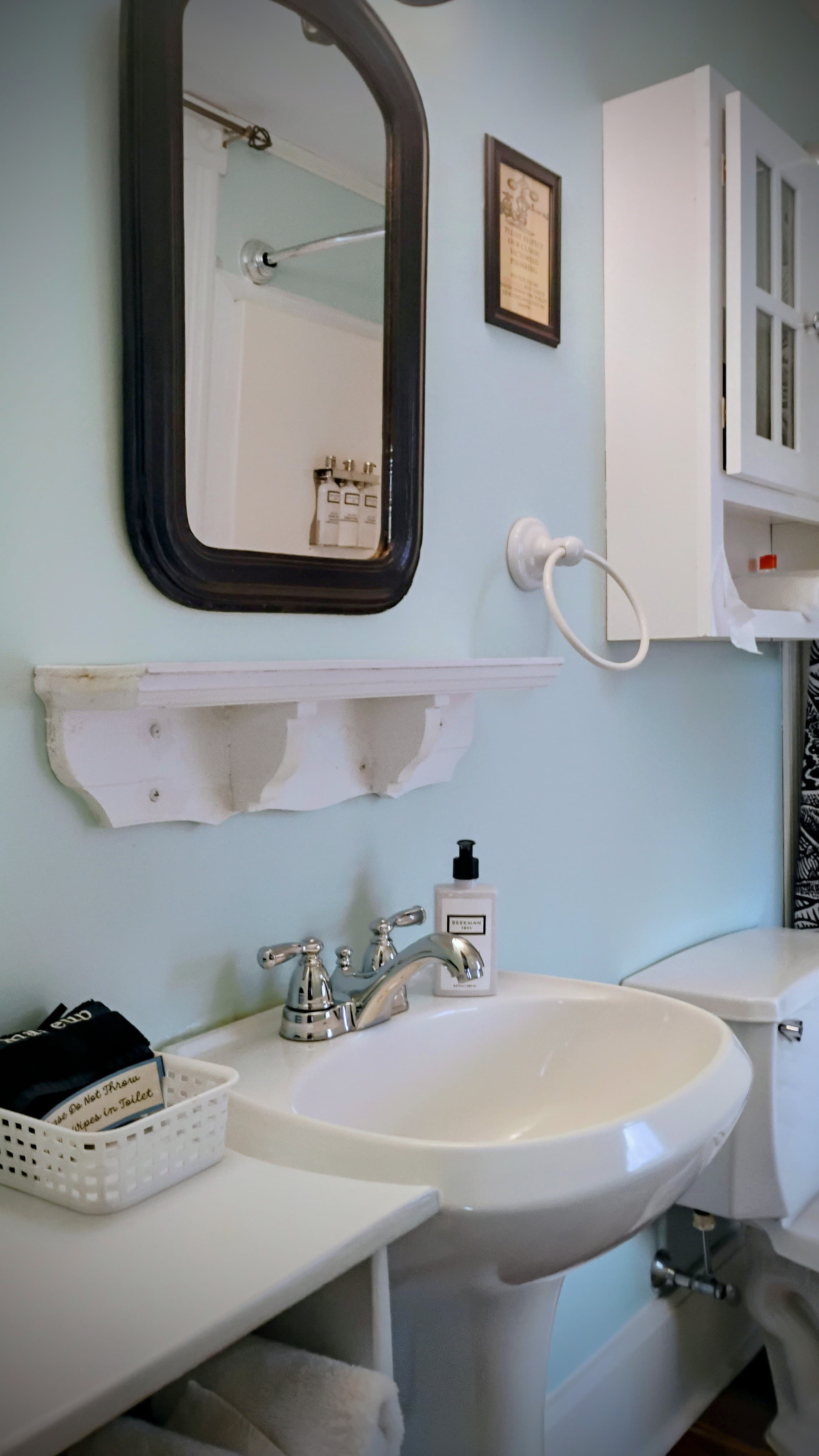 A modern bathroom featuring a sink, mirror, shelf, and toiletries against a pale blue wall.