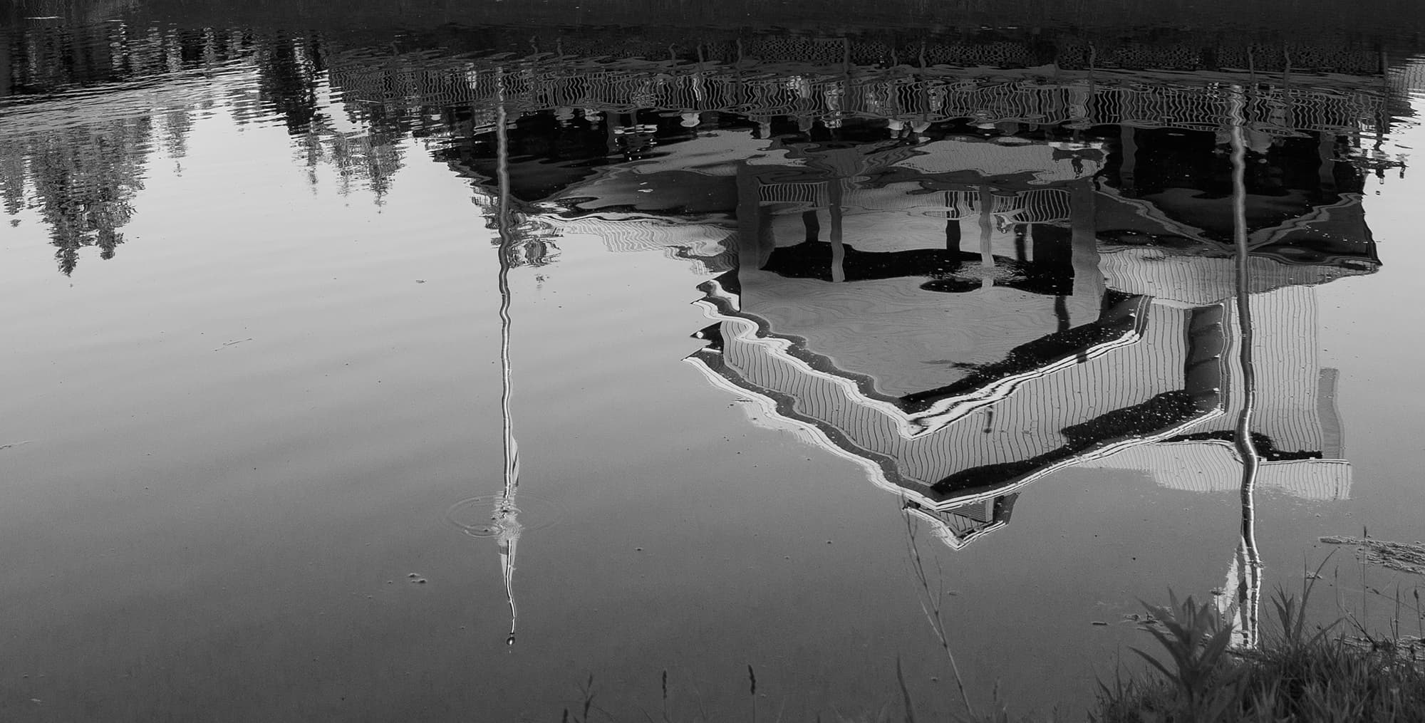 A black-and-white image of a building's distorted reflection in a calm body of water.