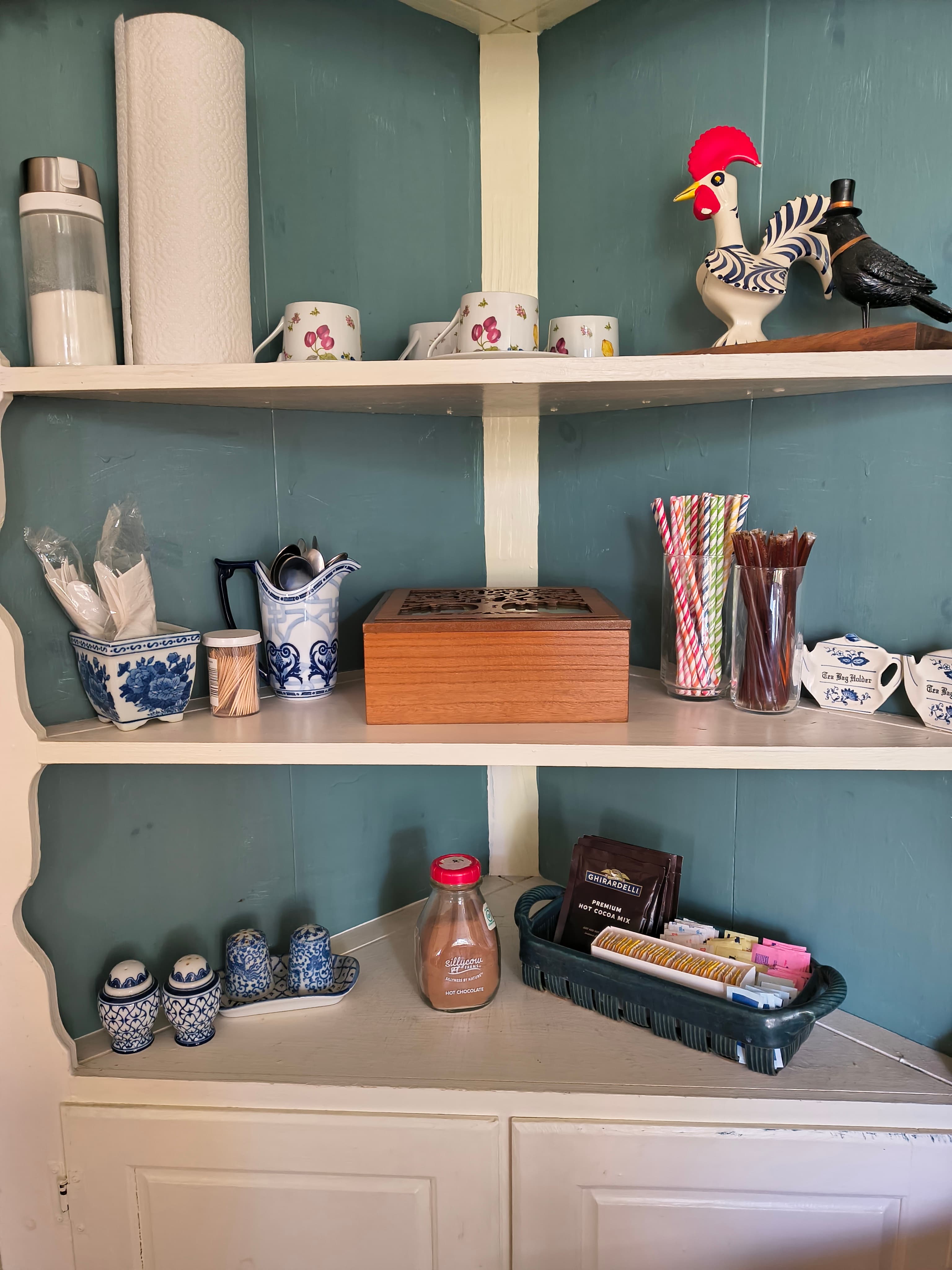 A wooden box and various labeled containers sit on a shelf alongside cups, utensils, and decorative items.