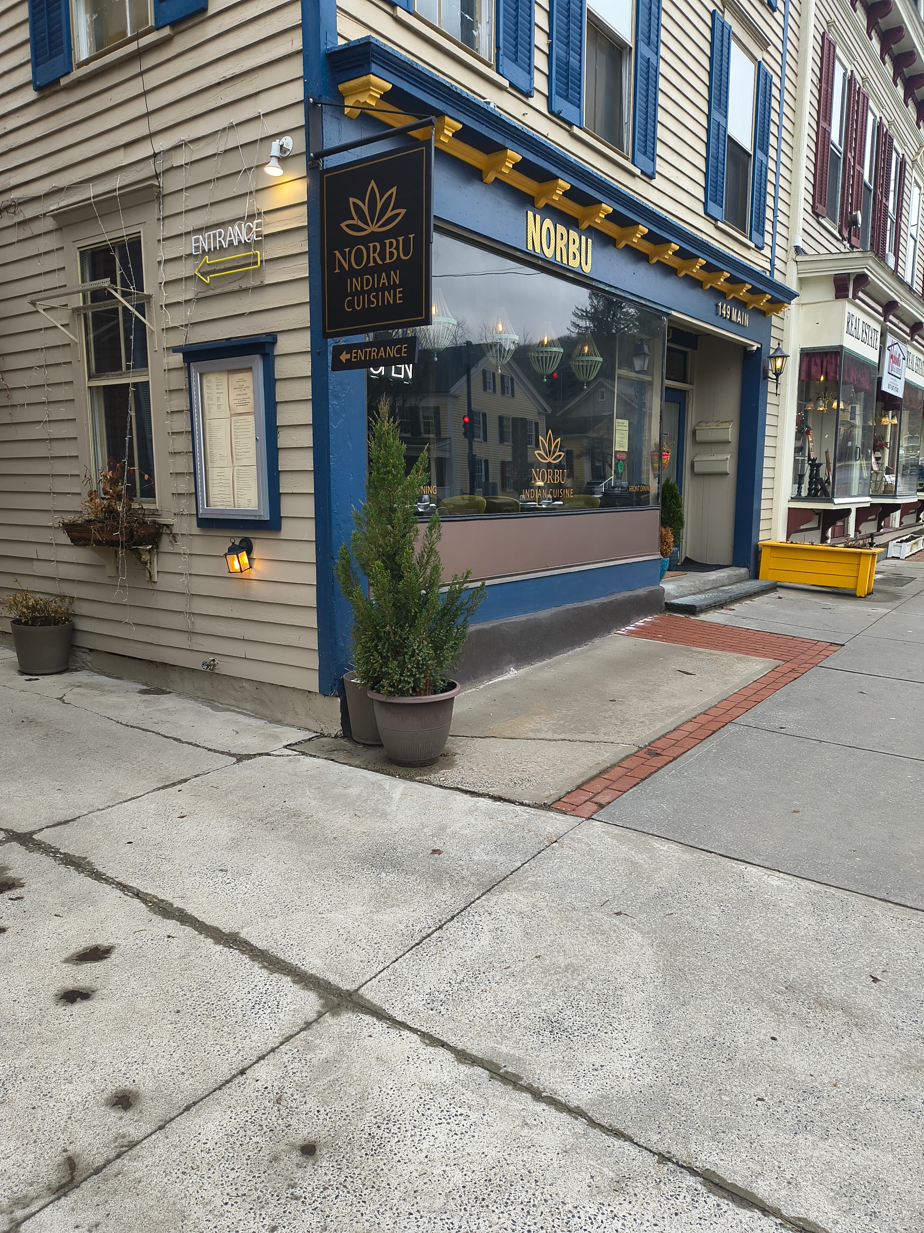 A corner restaurant titled "Norbu Indian Cuisine" features large windows and potted plants at the entrance.