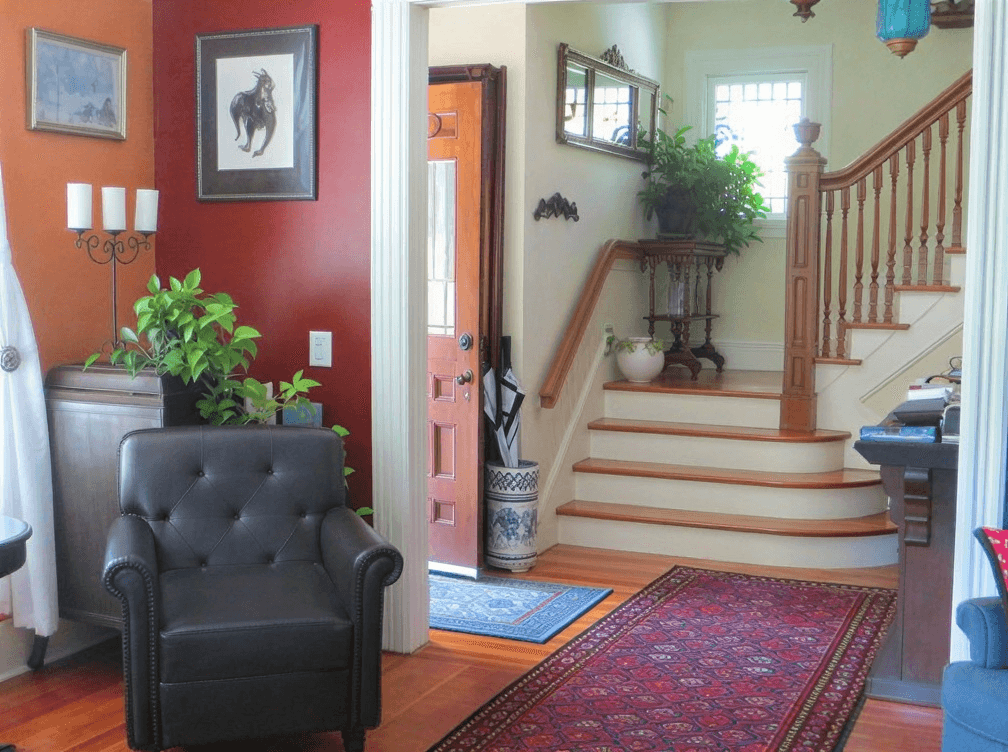 A cozy living area featuring a black armchair, red accent wall, and a staircase leading to a bright hallway.