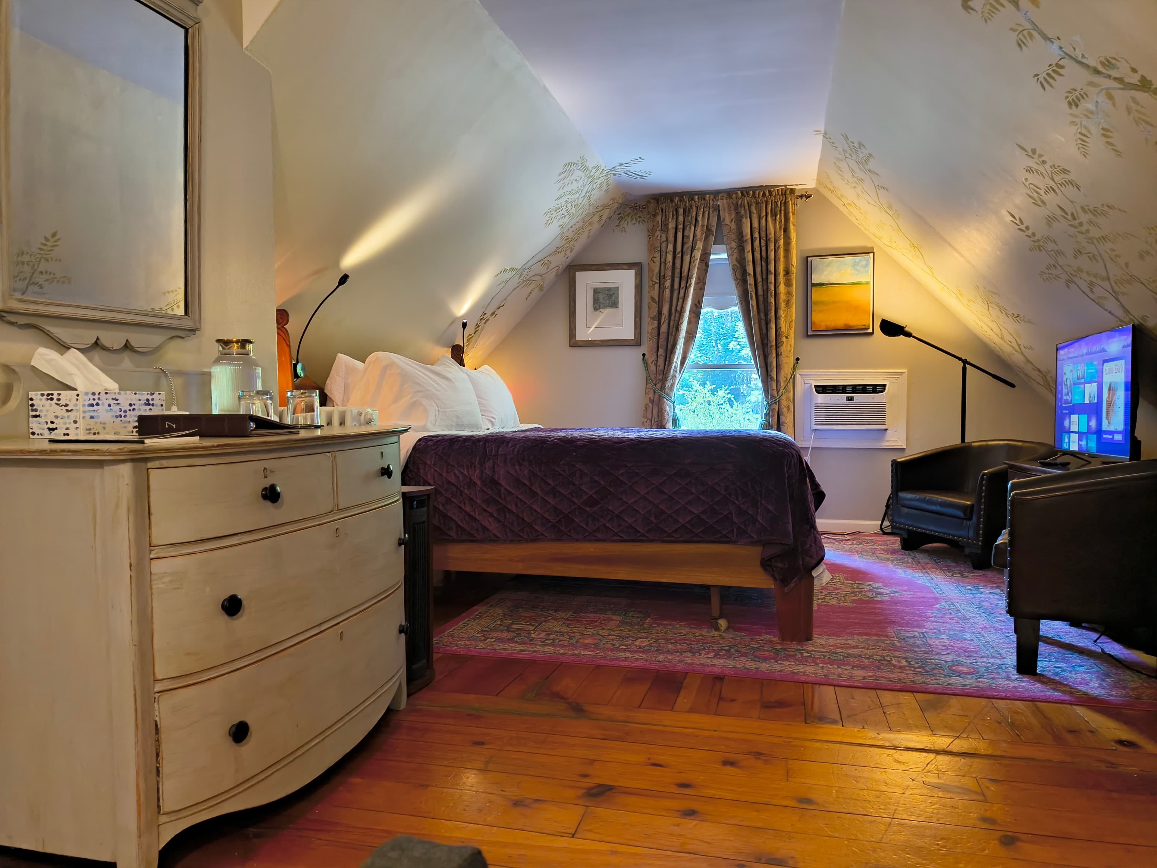 Cozy attic bedroom featuring a bed, dresser, television, and large window.
