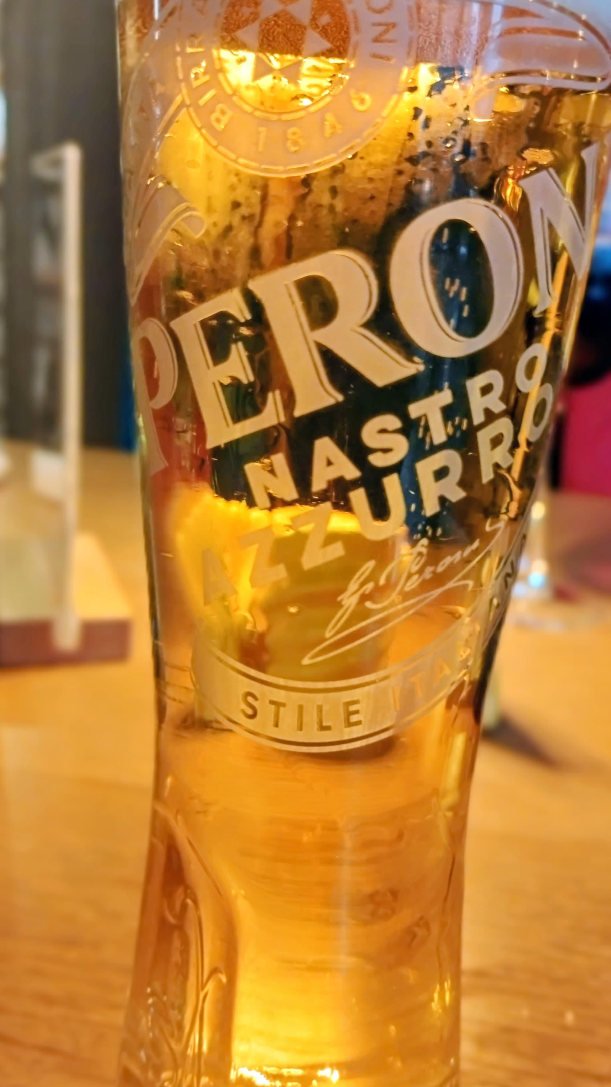 A close-up of a glass of Peroni Nastro Azzurro beer on a wooden table.