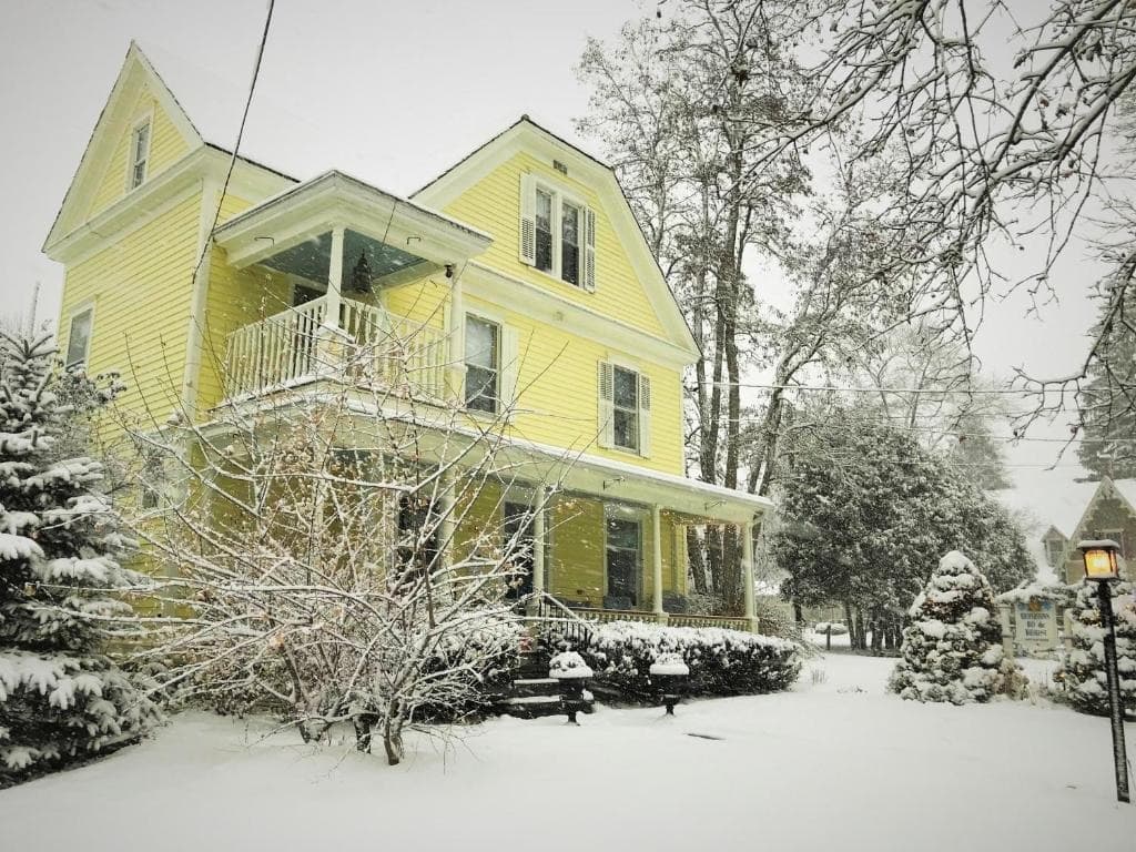 A yellow house surrounded by snow-covered trees and a white landscape.