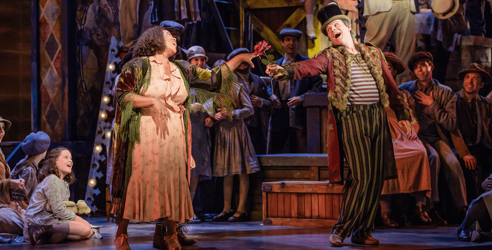 A musical performance featuring two lead characters singing, surrounded by an ensemble cast.