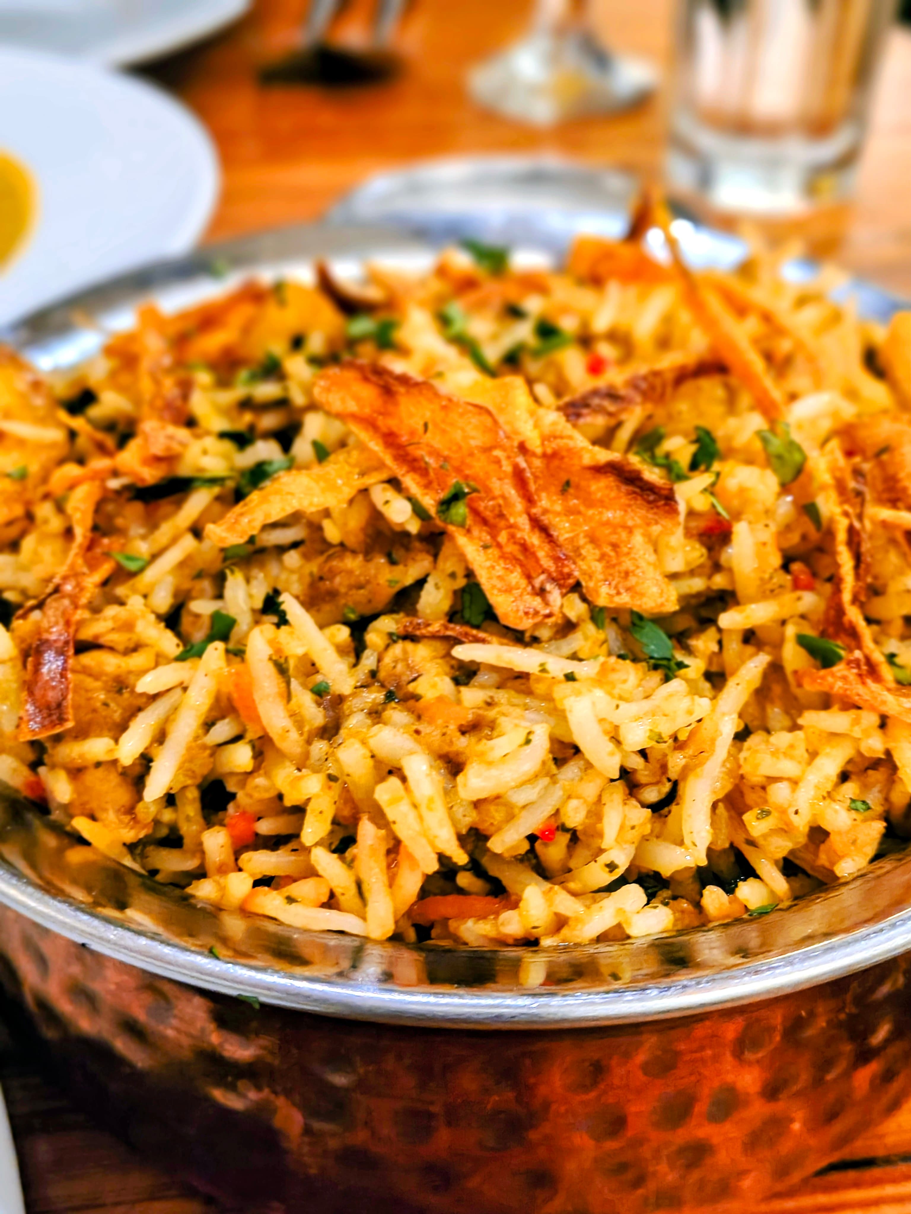A bowl of spiced biryani topped with crispy fried onions and herbs.