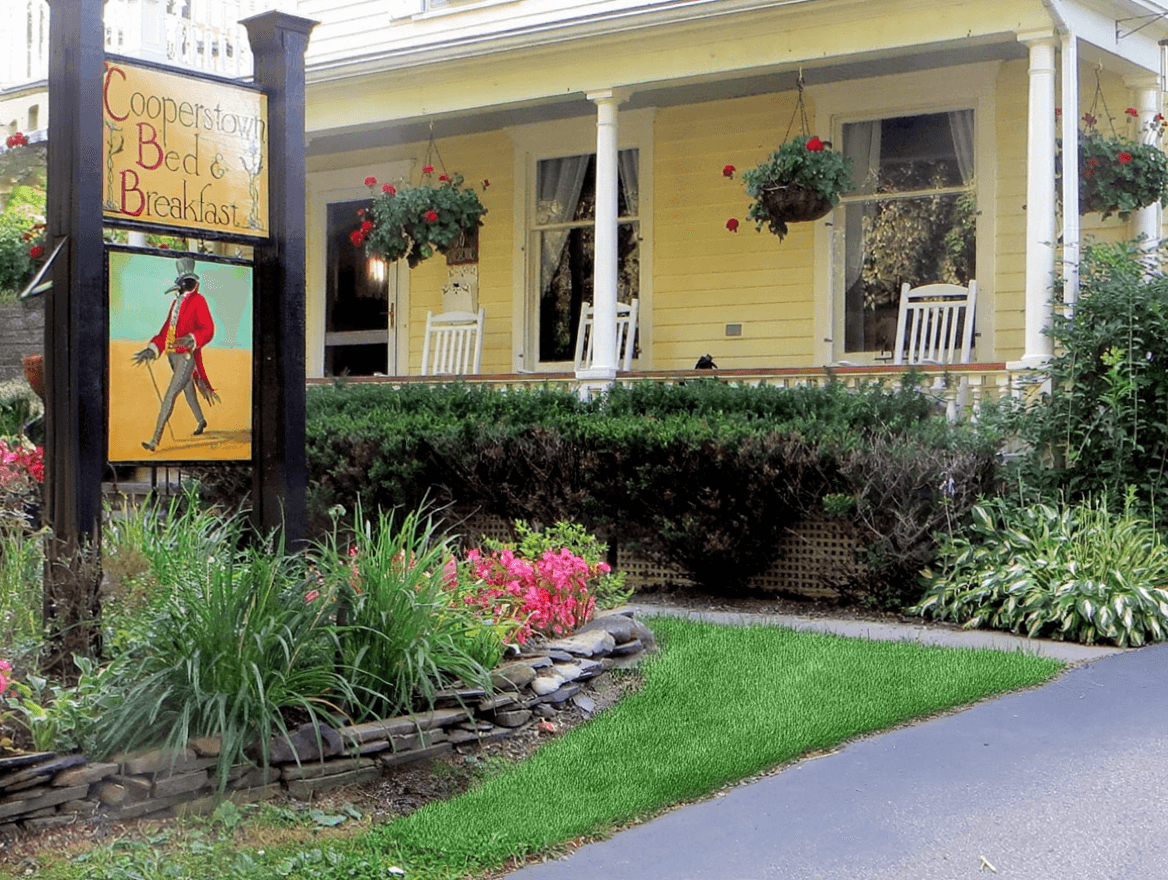 Entrance to Cooperstown Bed & Breakfast featuring a colorful sign and vibrant flowers.