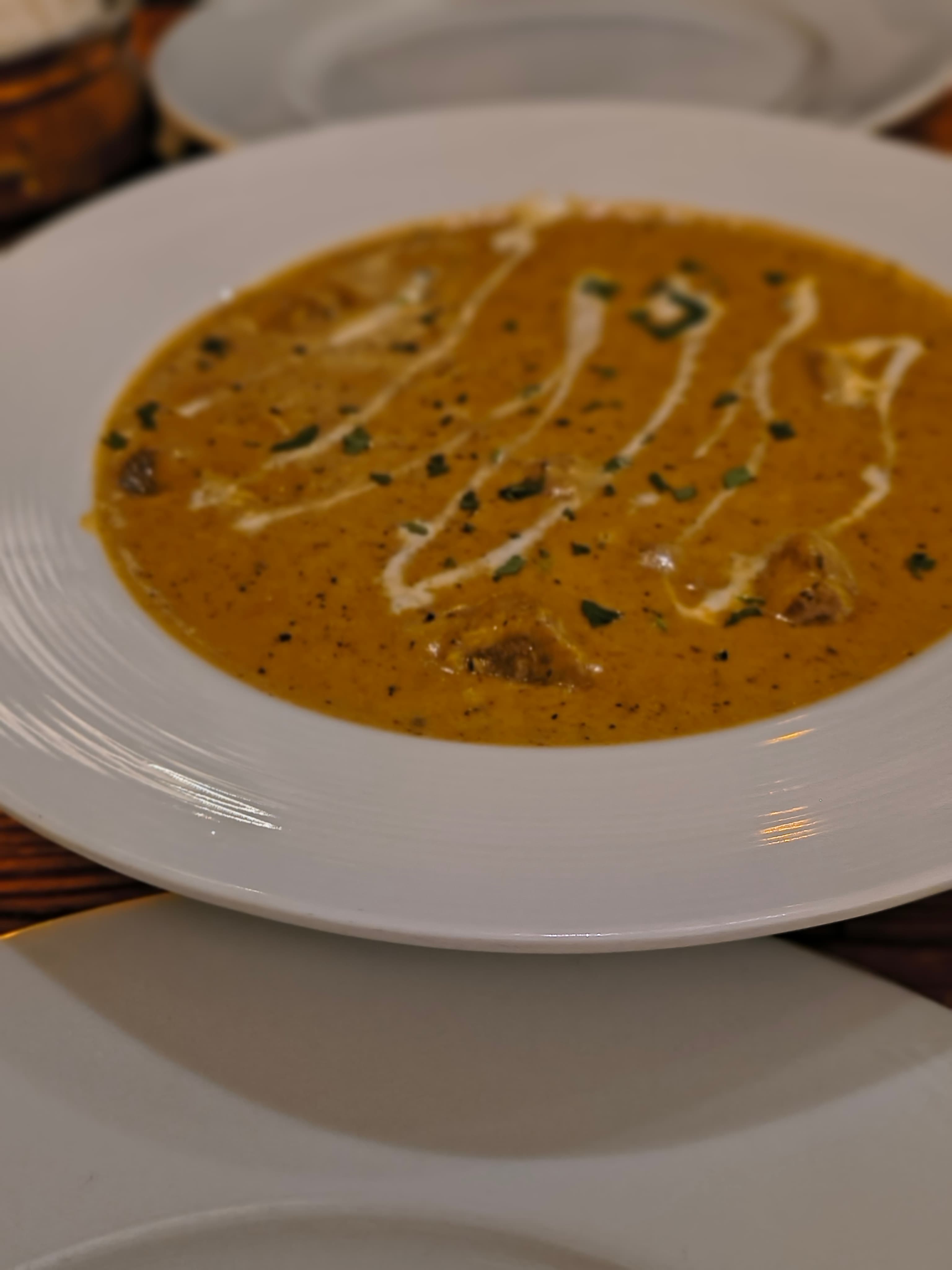 A bowl of creamy curry with drizzles of cream and green herbs on top.