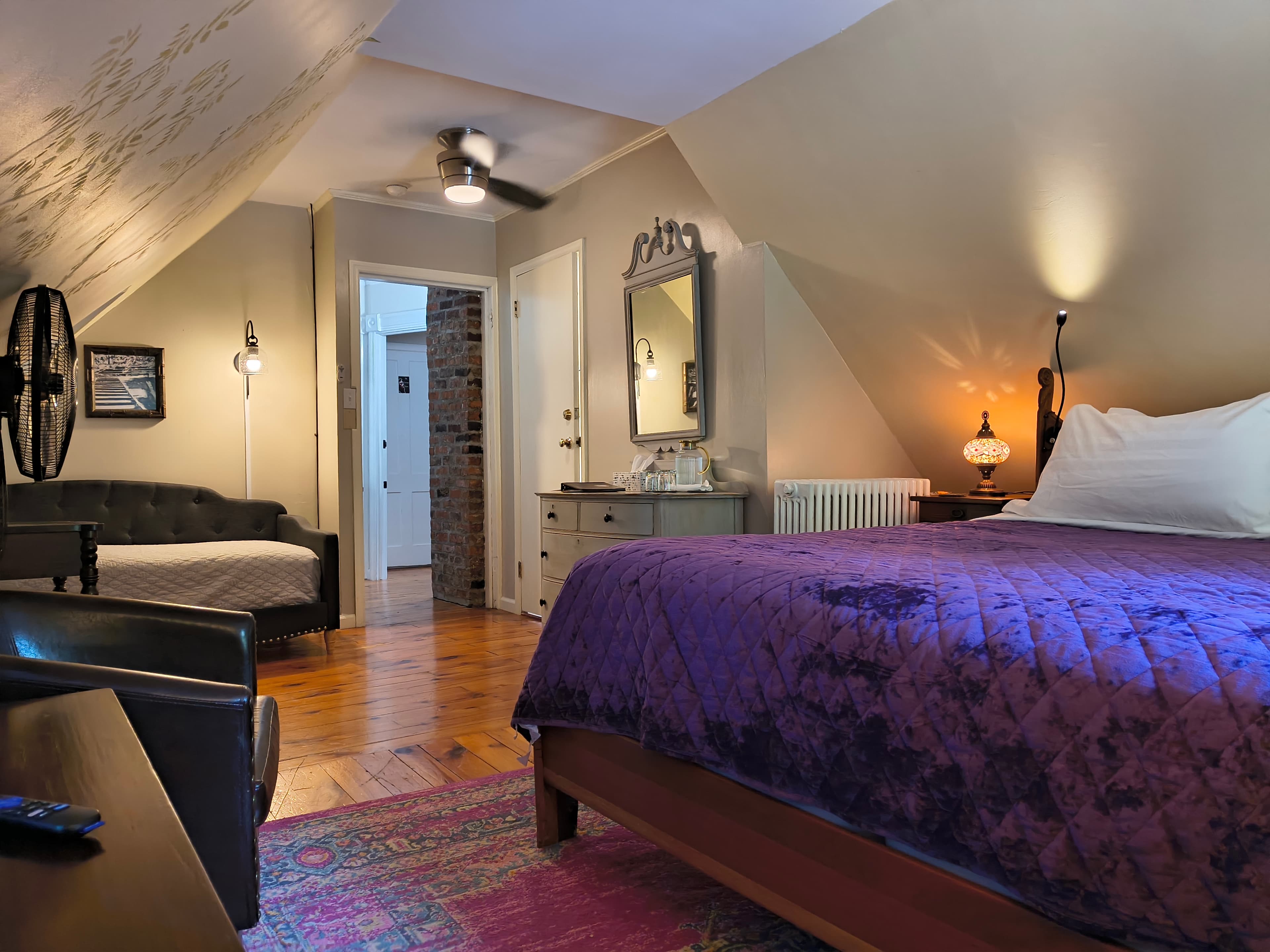 Cozy attic bedroom featuring a purple quilt, a sitting area, and warm lighting.